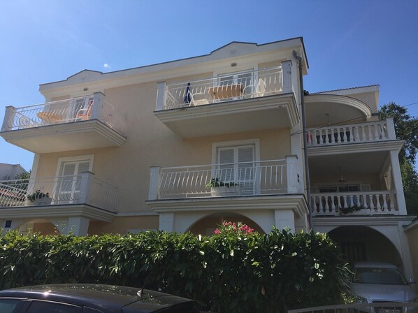 Un immeuble à plusieurs étages doté de balcons, une voiture garée devant et un arbuste au premier plan.