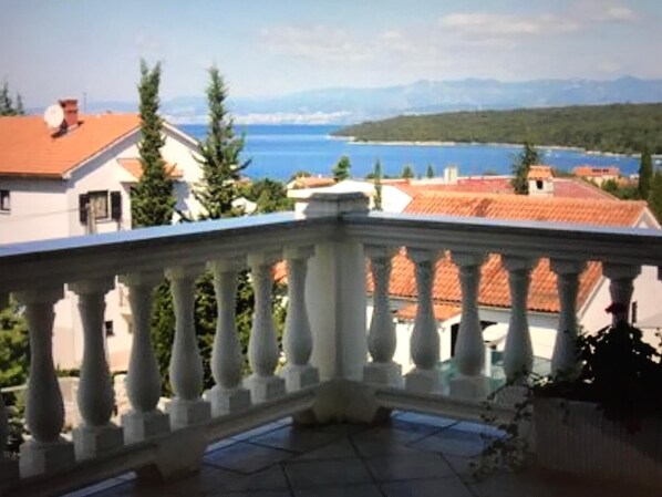 A balcony with a white balustrade overlooking a coastal area with buildings and a body of water.