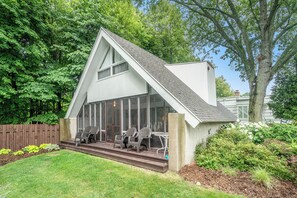 Une maison moderne dotée d’une grande baie vitrée, d’une terrasse en bois et d’un espace salon extérieur.