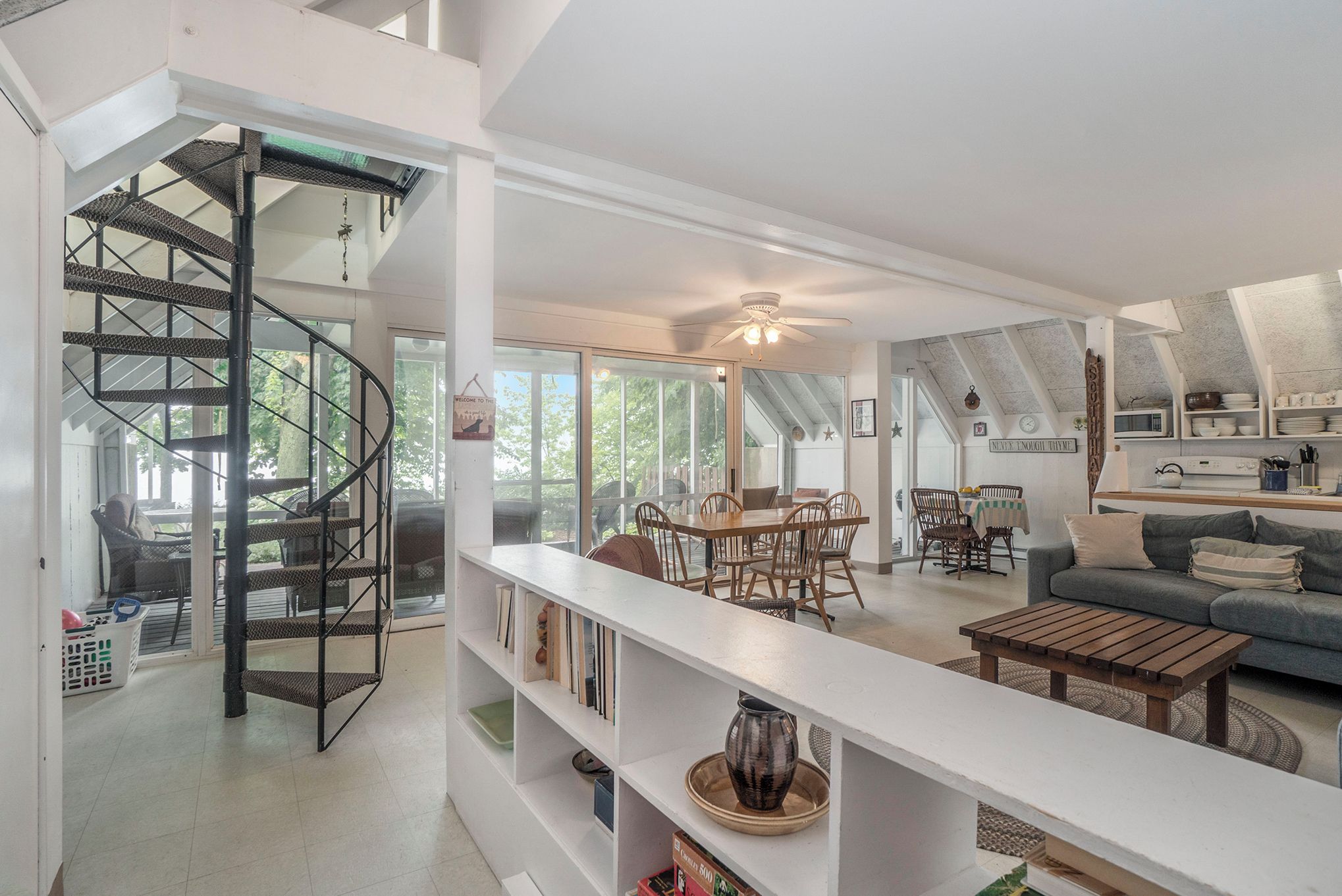 A spacious living area with a spiral staircase, a dining table with chairs, a sofa, and a ceiling fan.