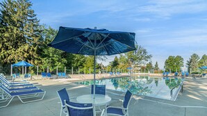 Zona de piscina con sillones de descanso y una mesa bajo una sombrilla grande.