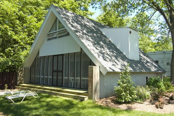 Une petite maison blanche, de plain-pied, avec un toit en pente et de grandes fenêtres.