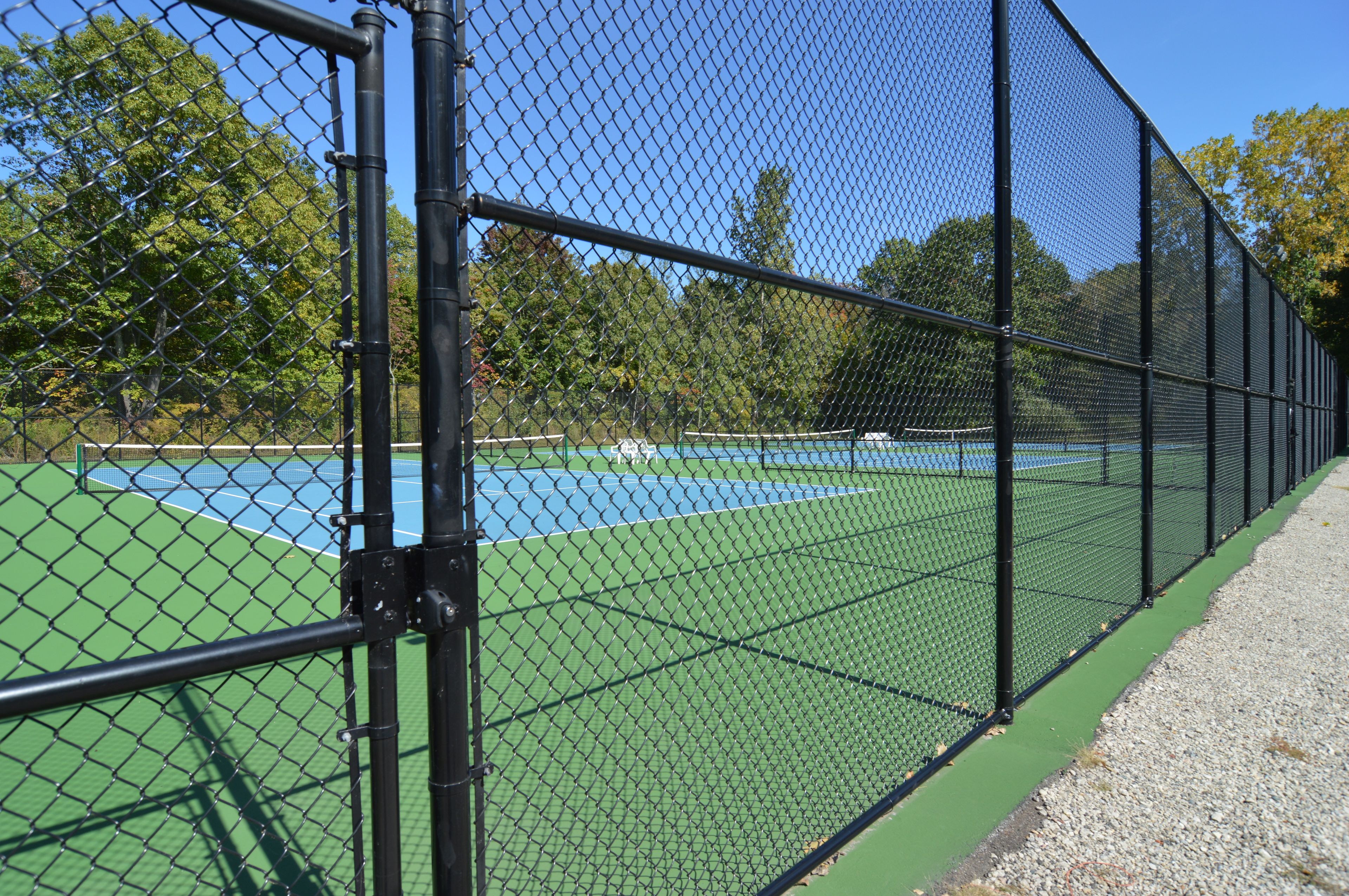 A tennis court enclosed by a chain-link fence with trees in the background.