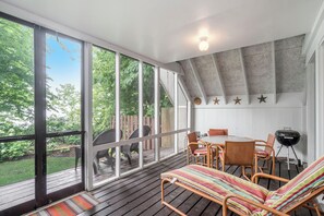 Une terrasse couverte avec une table et des chaises, un barbecue et une vue sur l’extérieur.