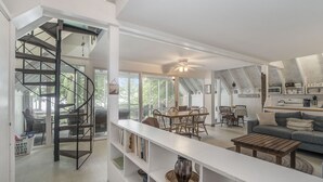 Amplia sala de estar con una escalera espiral, una mesa de comedor con sillas, un sofá y un ventilador de techo.