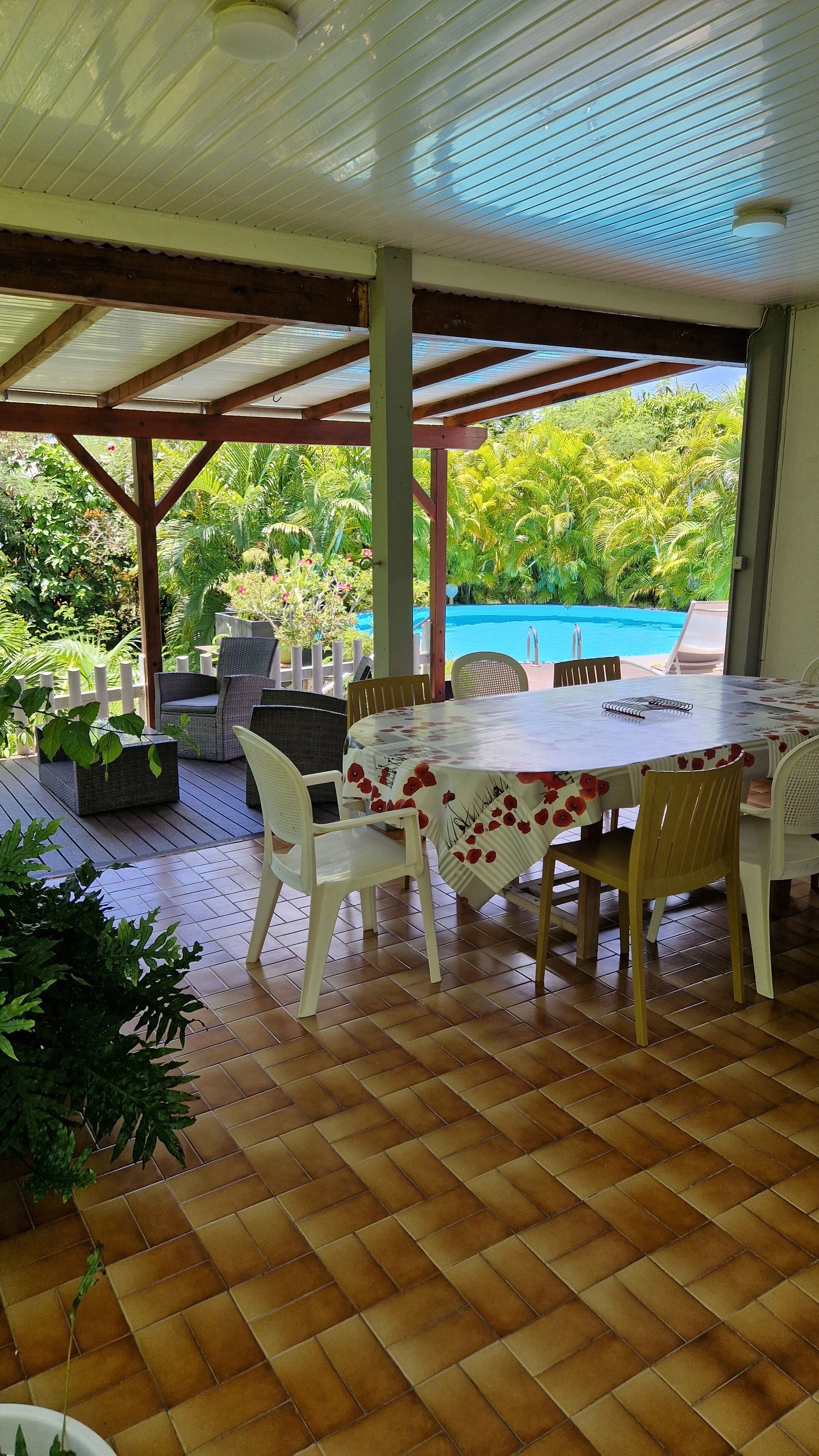 Eine Terrasse im Freien mit Tisch und Stühlen, ein Pool im Hintergrund und üppiges Grün.