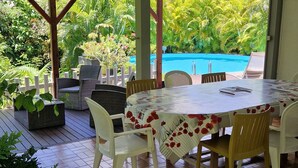 An outdoor patio with a table and chairs, a pool in the background, and lush greenery. - Villa Ti Colibri in Sainte-Anne 350 m from the sea (Sainte-Anne)