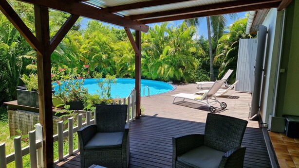 A covered outdoor area with a pool, wicker chairs, and a wooden deck. - Villa Ti Colibri in Sainte-Anne 350 m from the sea (Sainte-Anne)