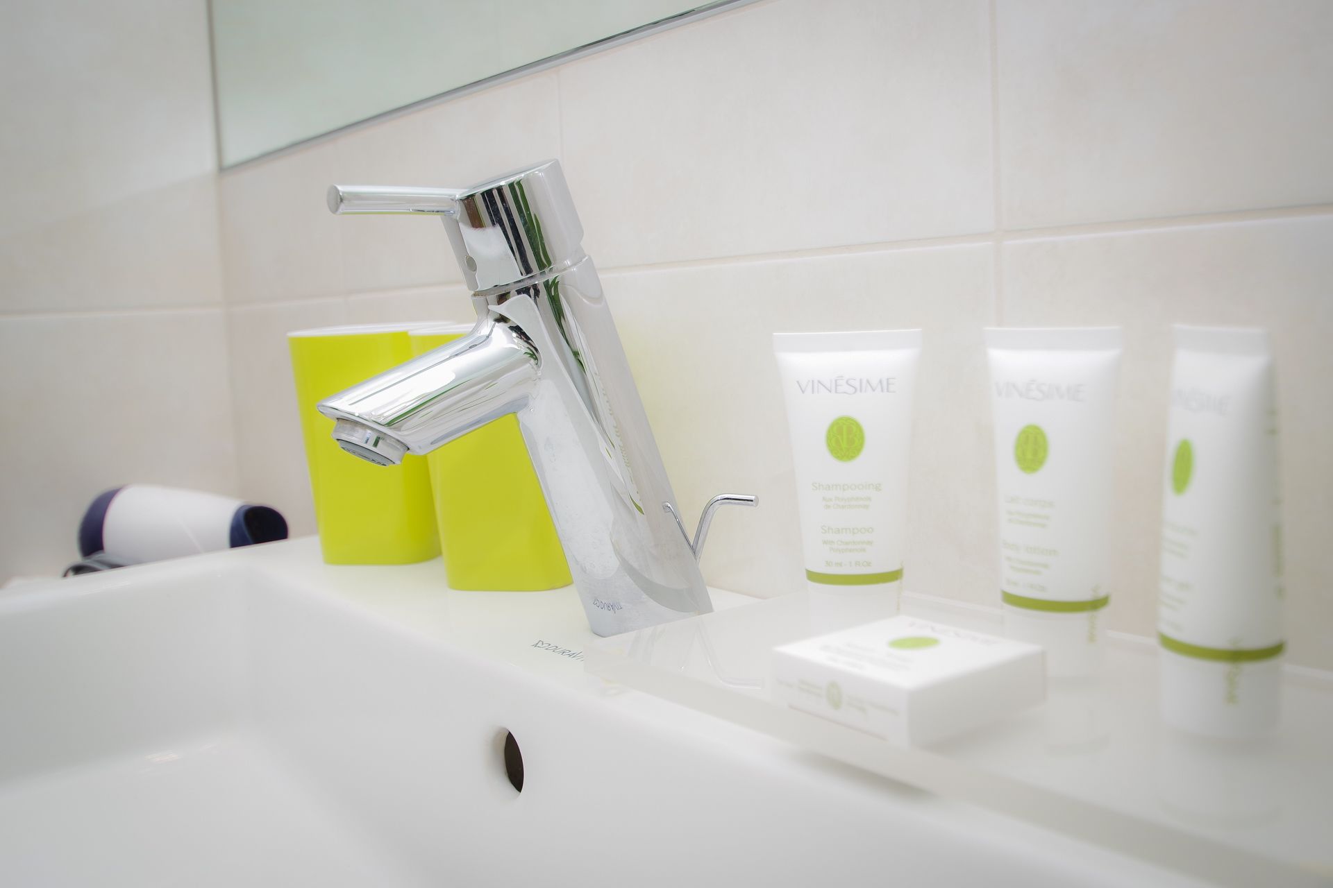 A bathroom with a modern chrome faucet, a white sink, and a row of toiletries including shampoo and conditioner.