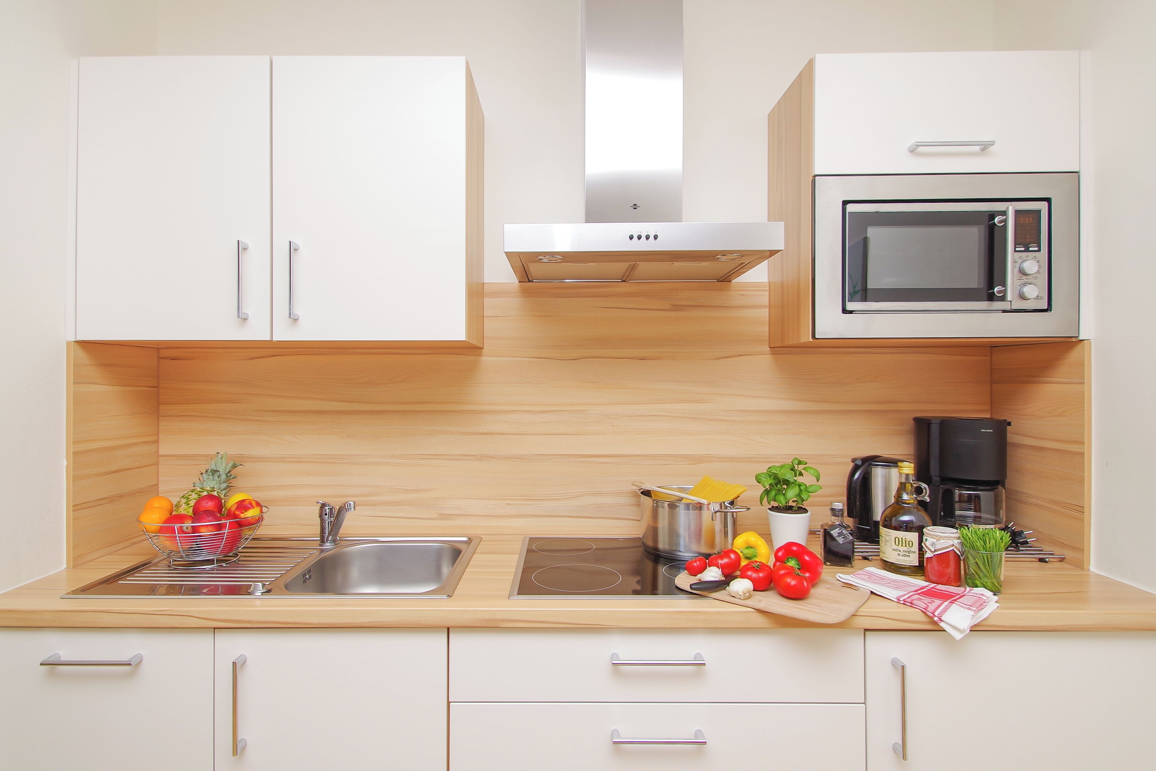 Cocina moderna con armarios blancos, un lavamanos de acero inoxidable, un microondas y una cafetera.