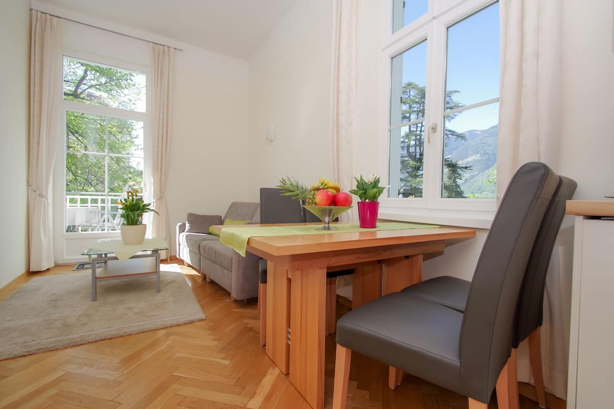 Un espace de salle à manger moderne, avec une table en bois, des chaises à revêtement gris et une vue sur les arbres à travers de grandes fenêtres.