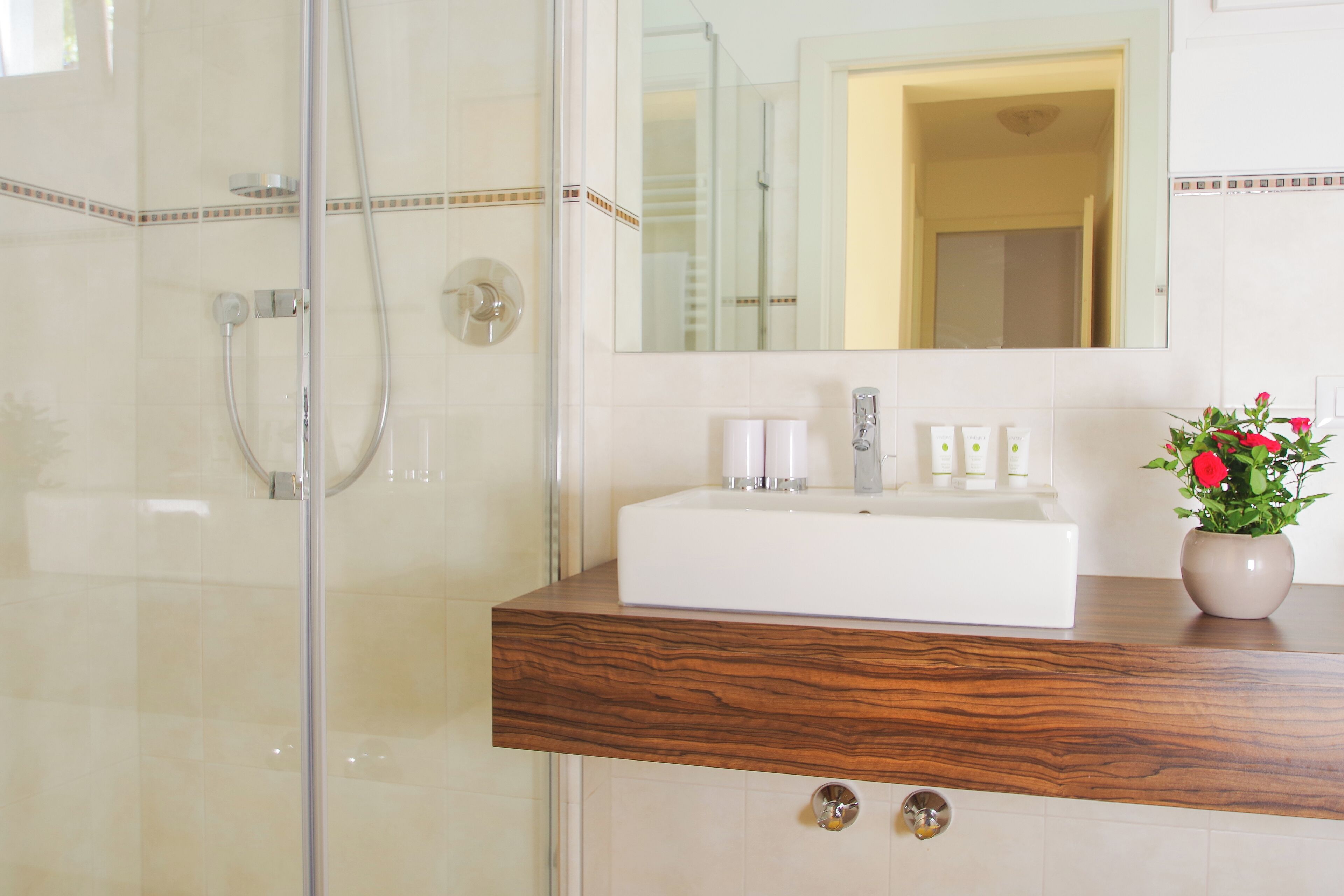 Une salle de bain avec une douche à parois de verre, un lavabo blanc doté d’un plan de toilette en bois et un miroir au-dessus du lavabo.