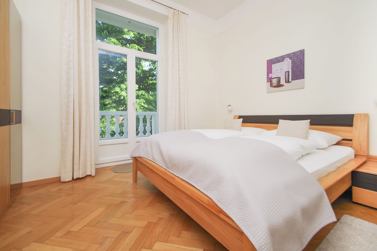 Une chambre avec un lit en bois, une fenêtre avec des rideaux et un tableau accroché au mur.