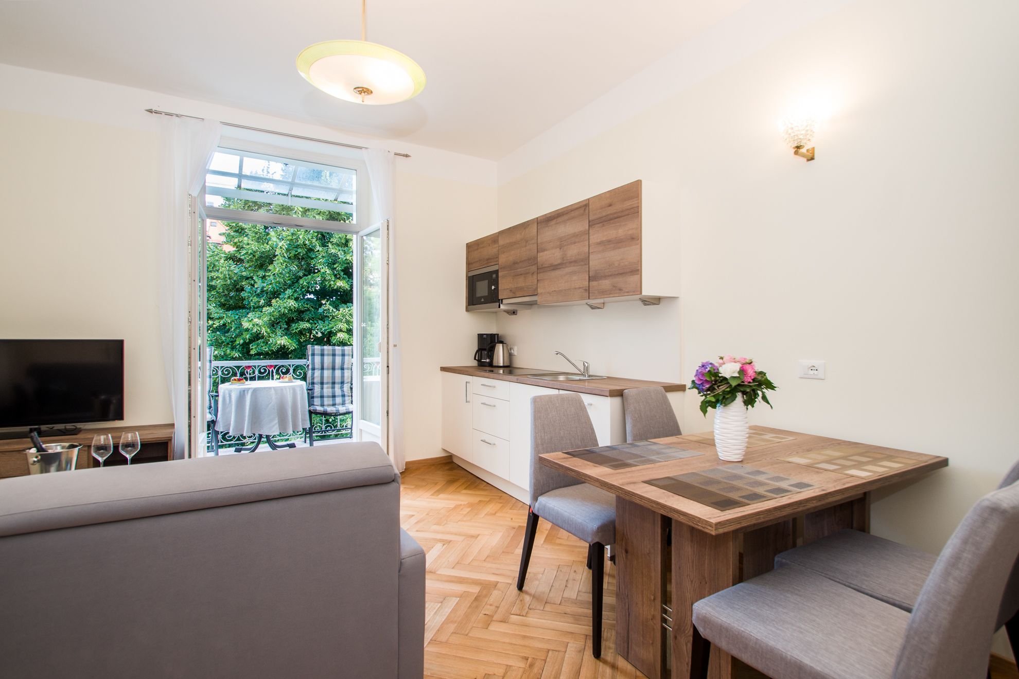 Een compacte keuken met een eethoek, een televisie en een balkon met uitzicht op groen.