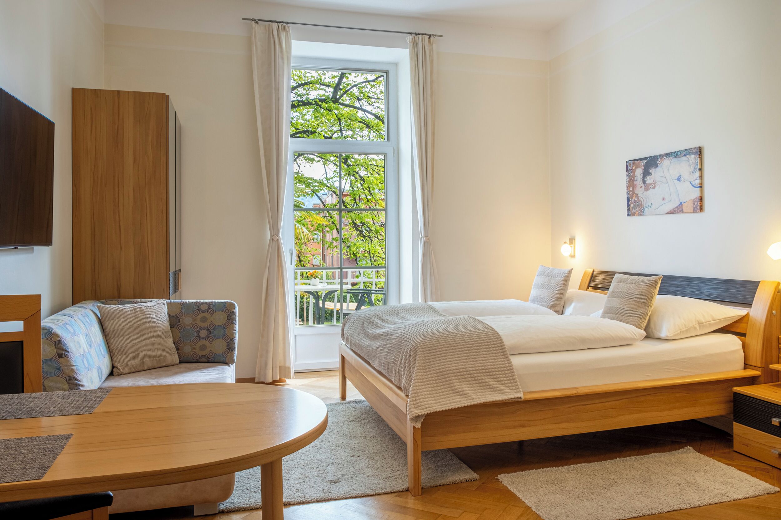 Un dormitorio con cama, sofá, mesa y ventana con cortinas.