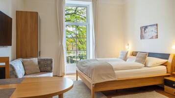 Un dormitorio con cama, sofá, mesa y ventana con cortinas.