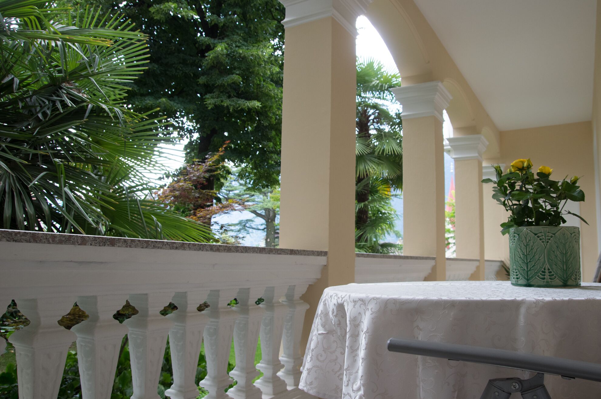 A balcony with a white railing, a table with a white tablecloth, and a potted plant with yellow flowers.