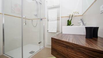 A modern bathroom with a glass shower enclosure, a wooden vanity with a sink, and a small green rug.