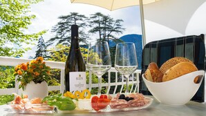 A table set with a bottle of wine, glasses, a bowl of bread, and a charcuterie board with various meats and vegetables. - Residence Diana (Merano)