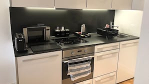 Eine moderne Küche mit schwarzer Arbeitsplatte, integriertem Backofen, Mikrowelle und Wasserkocher. Darüber befinden sich Schränke und ein Handtuch hängt am Backofen-Griff.