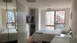 Ein modernes Schlafzimmer mit zwei Betten, einem Fernseher und einem großen Fenster mit Blick auf die Stadt.