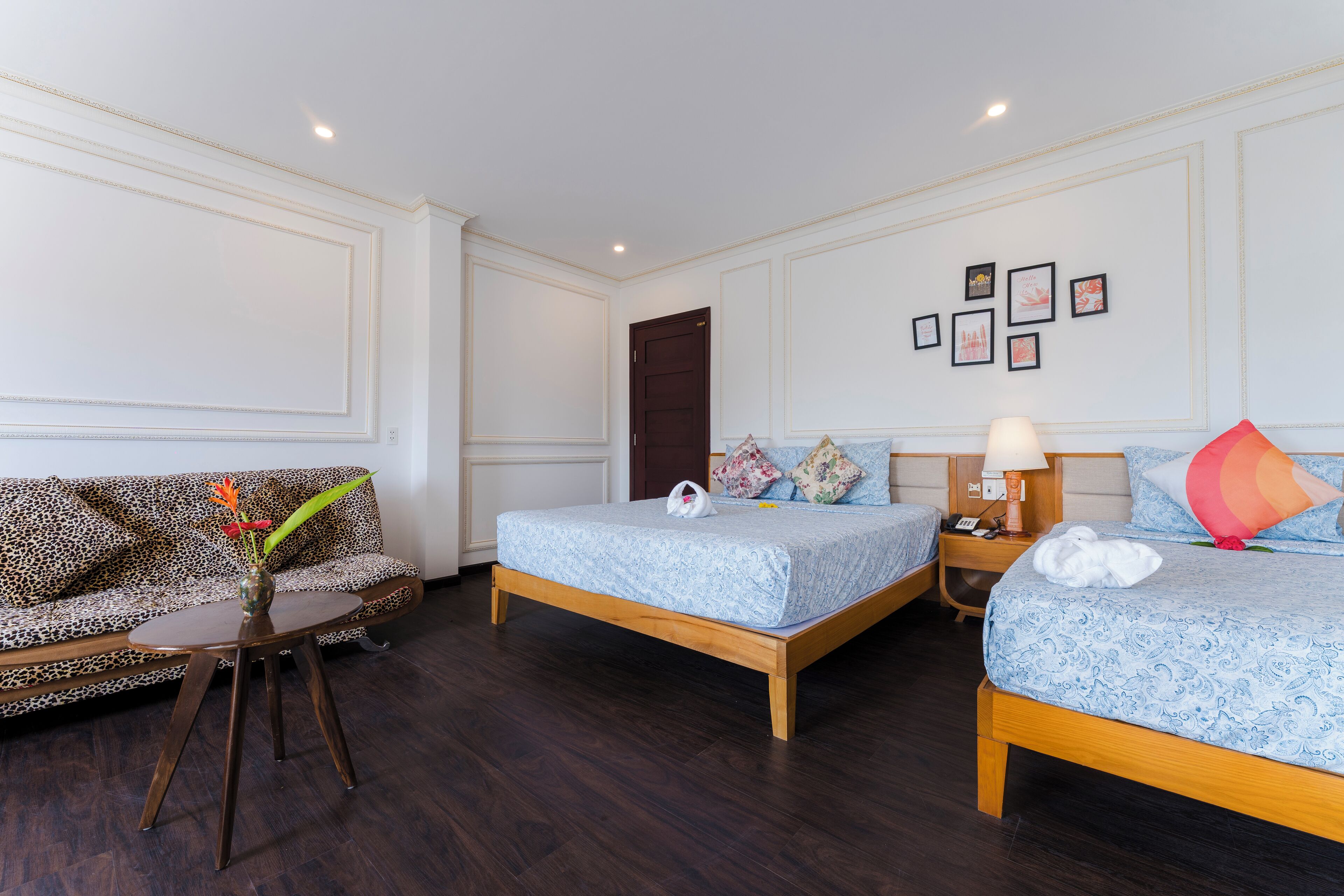 A hotel room with two beds, a sofa, a small table, and a vase with flowers.