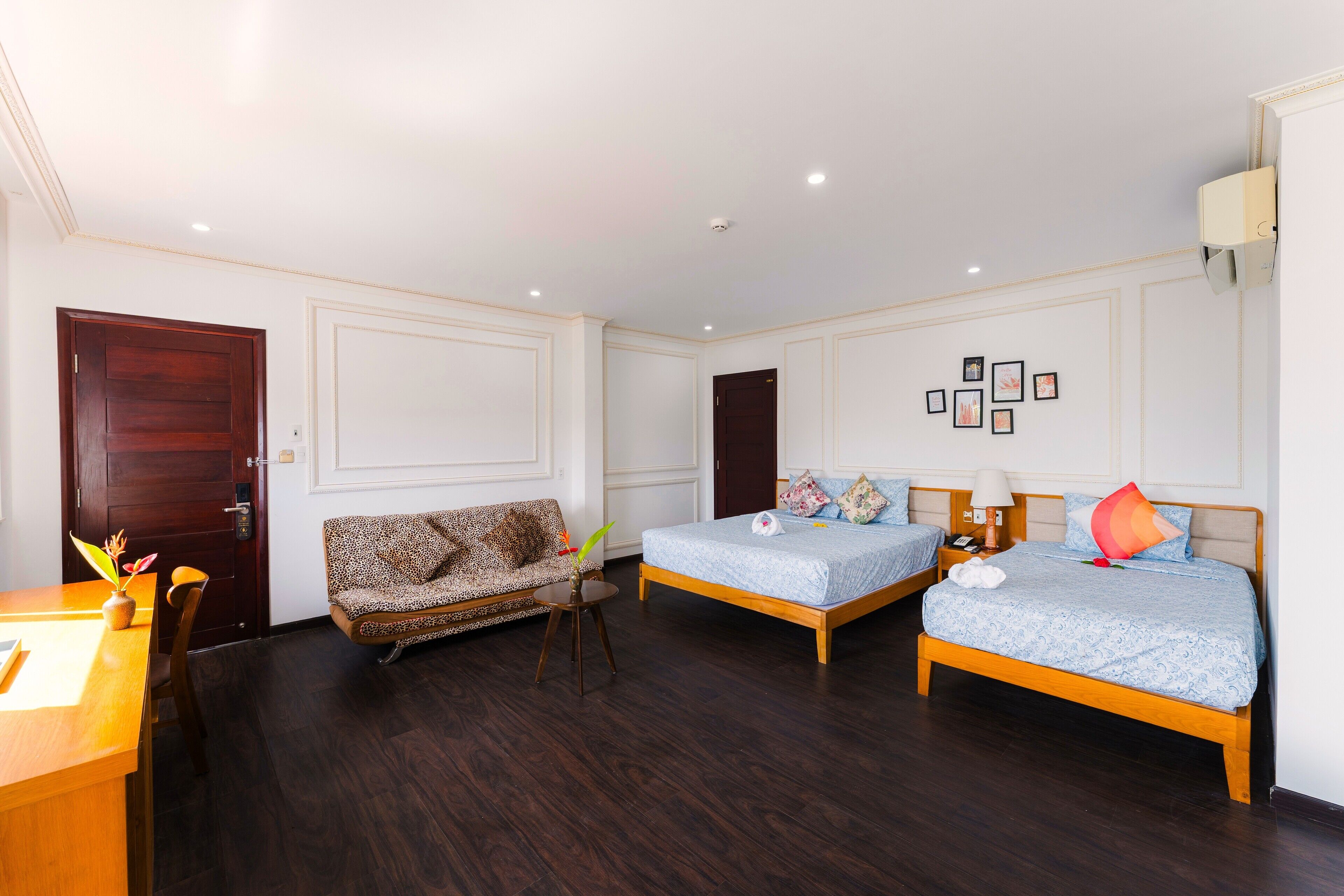 A hotel room with two beds, a sofa, a desk, and a small table with a plant.
