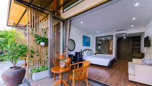 Quarto de hotel moderno com cama, sofá, mesa de jantar com cadeiras e uma grande planta em vaso.