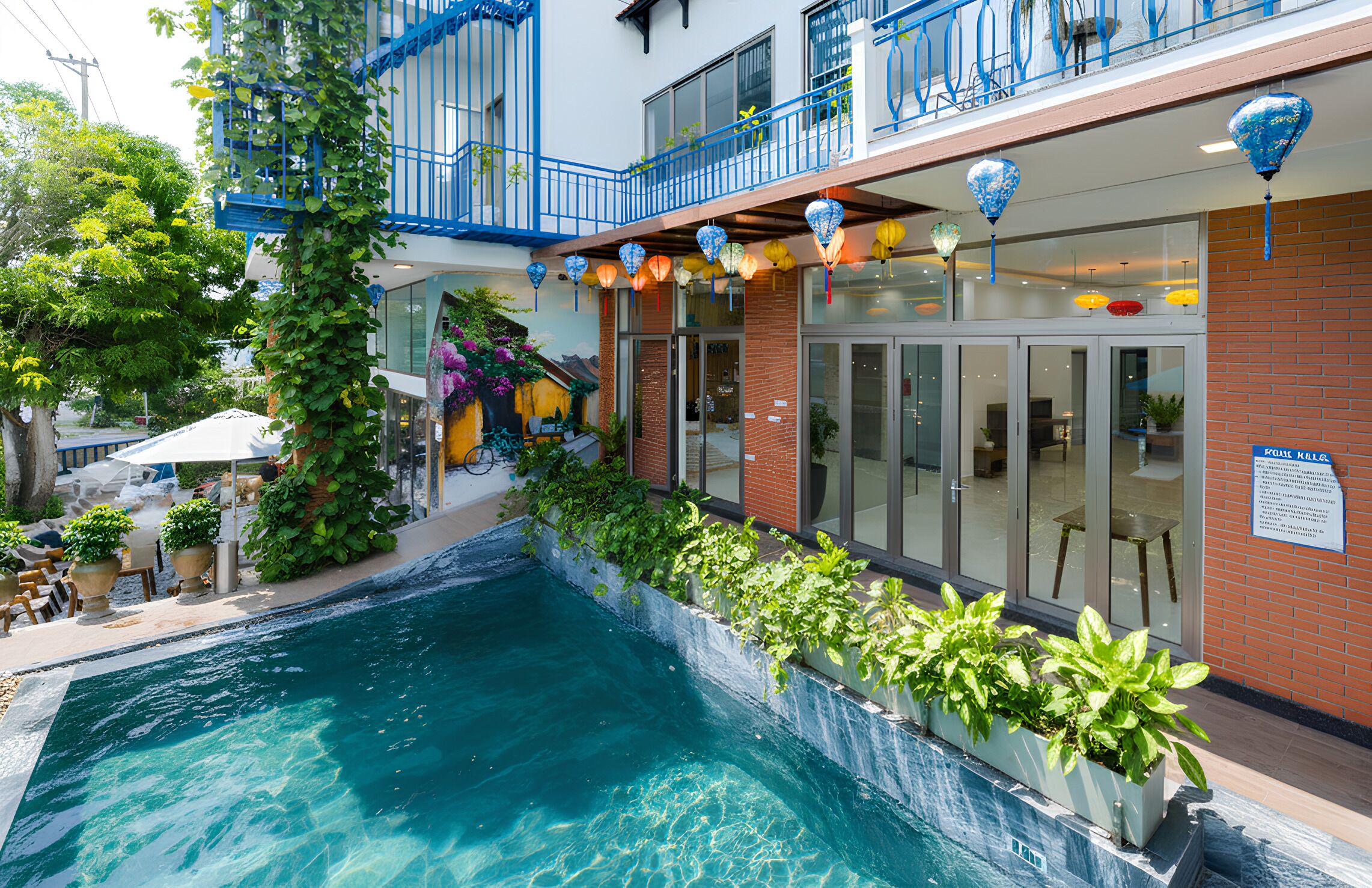 A hotel with a swimming pool, outdoor seating, and a balcony with blue railings.