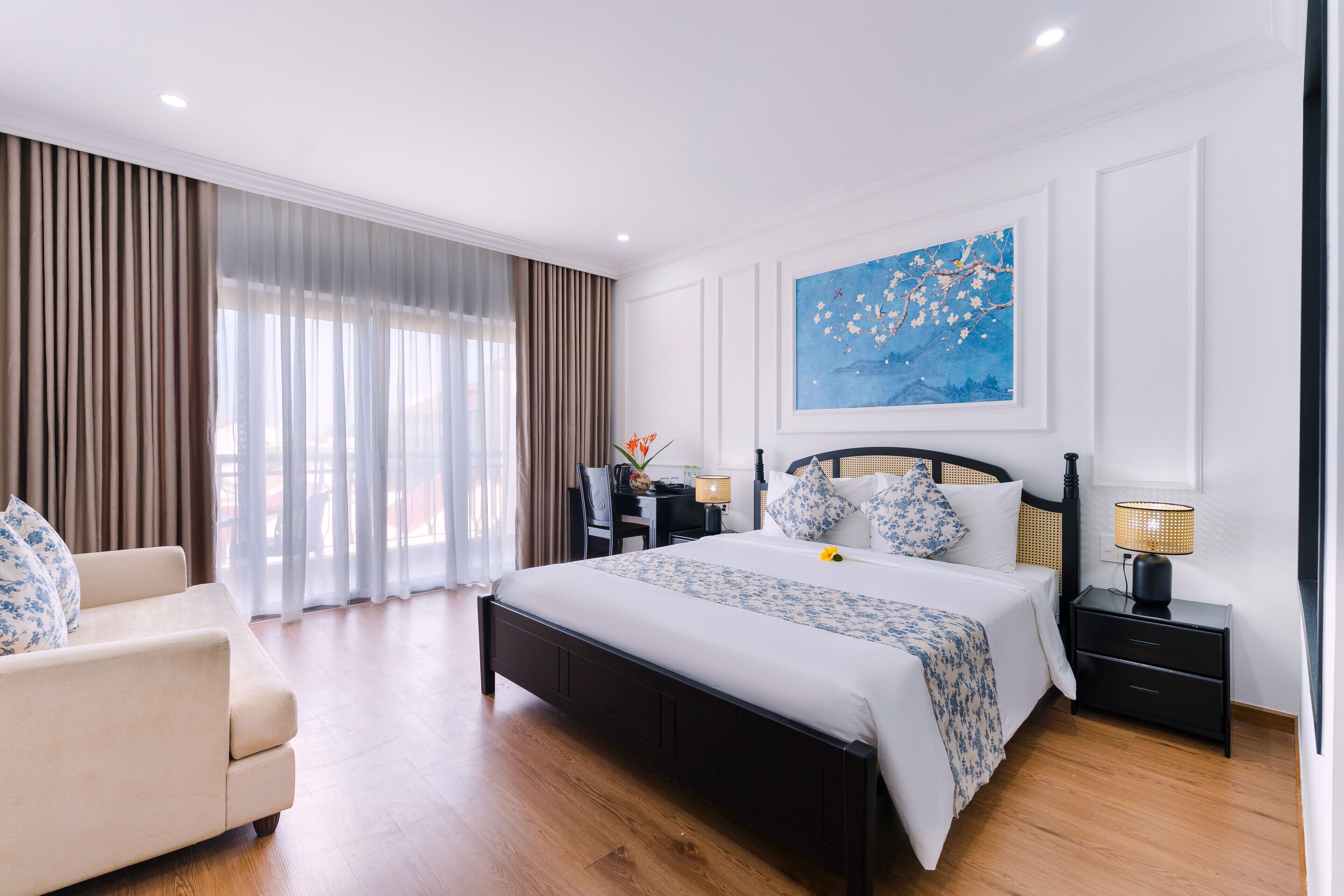 A modern hotel room with a large bed, a sofa, a desk, and a nightstand.