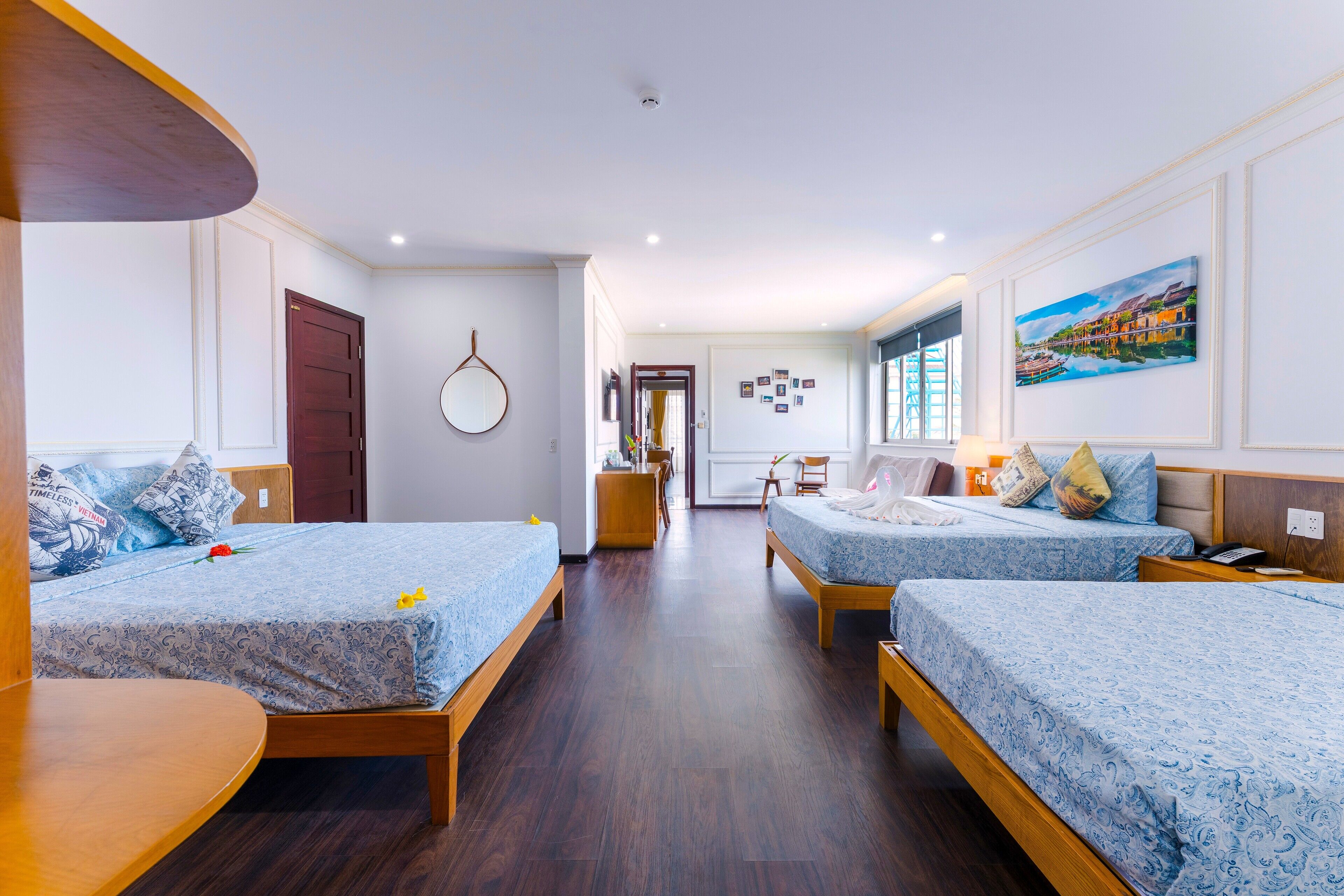 A hotel room with two beds, a wooden desk, a mirror, and a painting on the wall.