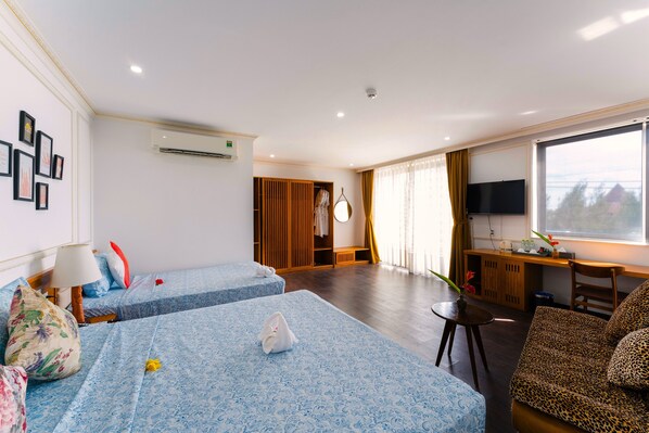 A hotel room with two beds, a sofa, a desk with a TV, and a large window.