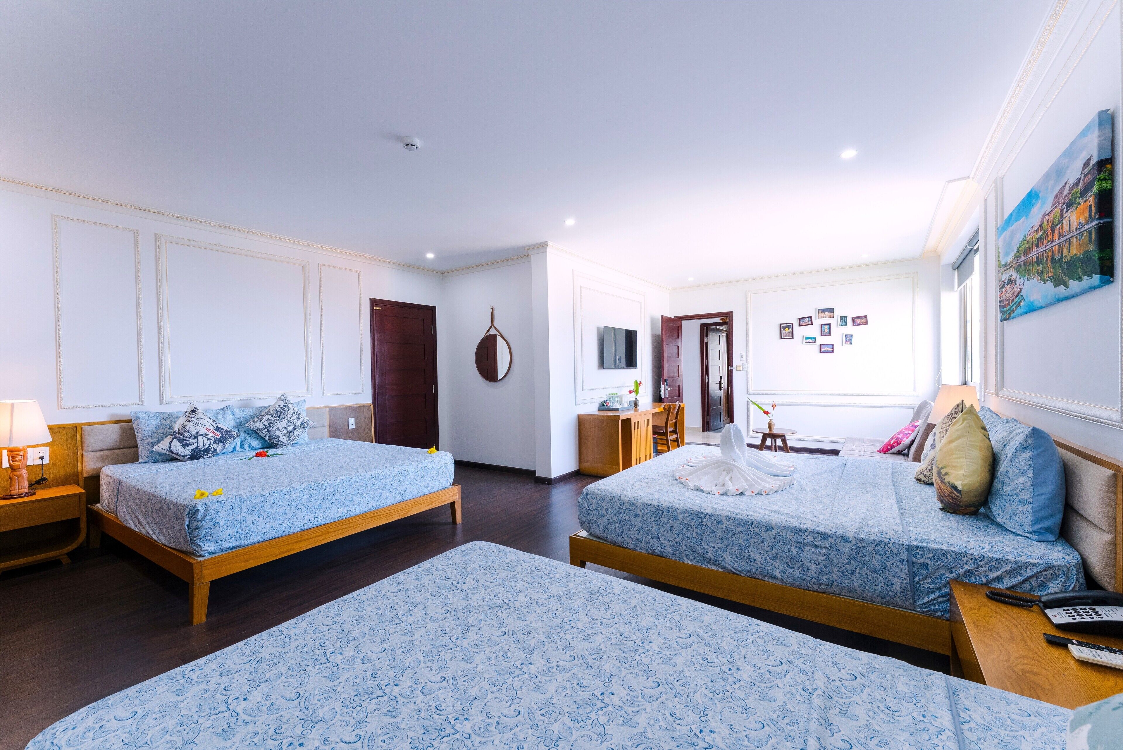 A hotel room with two beds, a desk, a chair, a TV, and a painting on the wall.