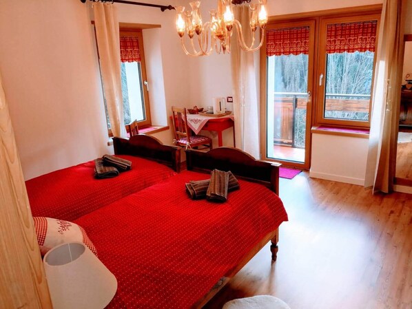 Quarto com duas camas, uma mesa de jantar, cadeiras, um candelabro e varanda com vista.