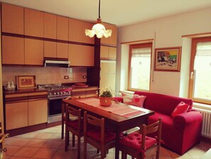 Uma cozinha compacta com armários de madeira, fogão a gás e um sofá vermelho.