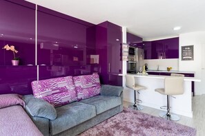 Una sala de estar moderna con un sofá gris, cojines morados y una pequeña zona de bar con taburetes.