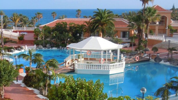 Un resort con piscina central, palmeras y vista al océano.