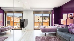 Una sala de estar moderna con un televisor grande, un sofá, una cama y un balcón con vistas a edificios.