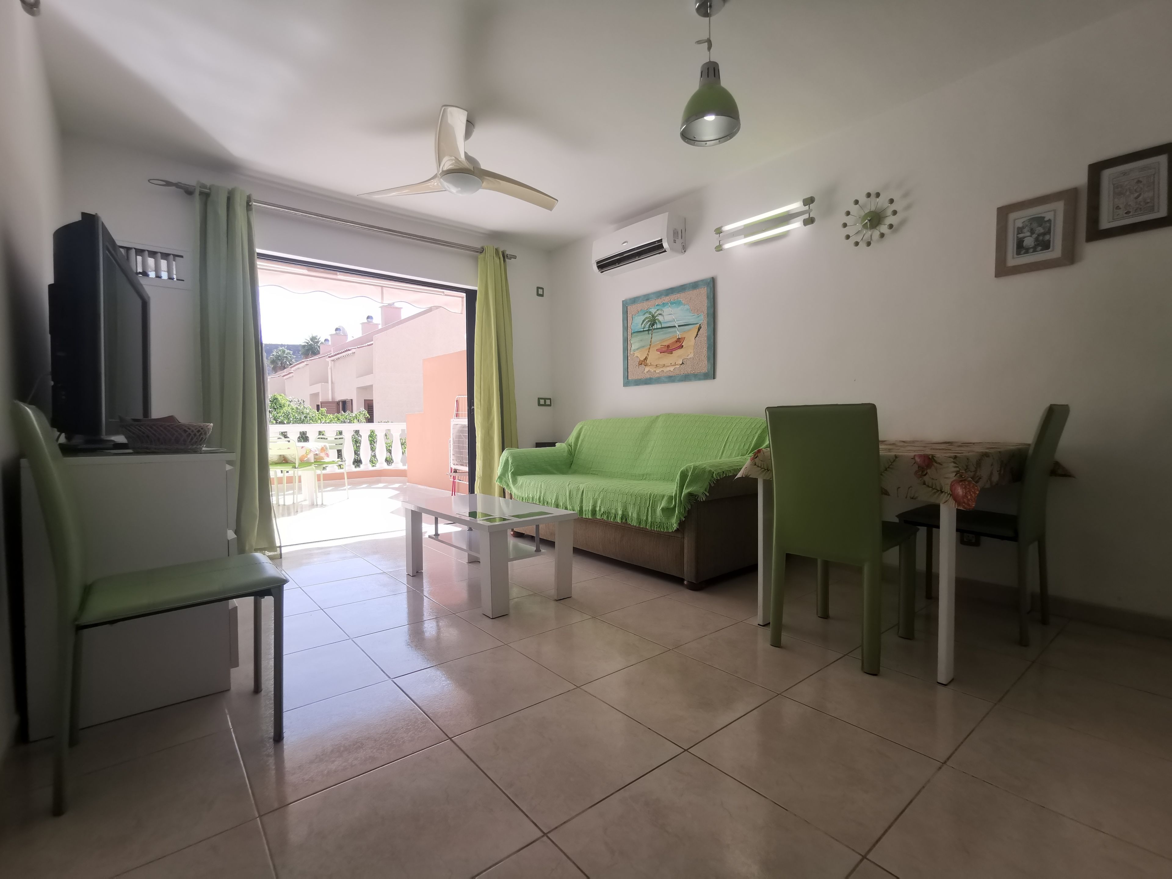 A living room with a sofa, chairs, a table, a ceiling fan, and an air conditioning unit.