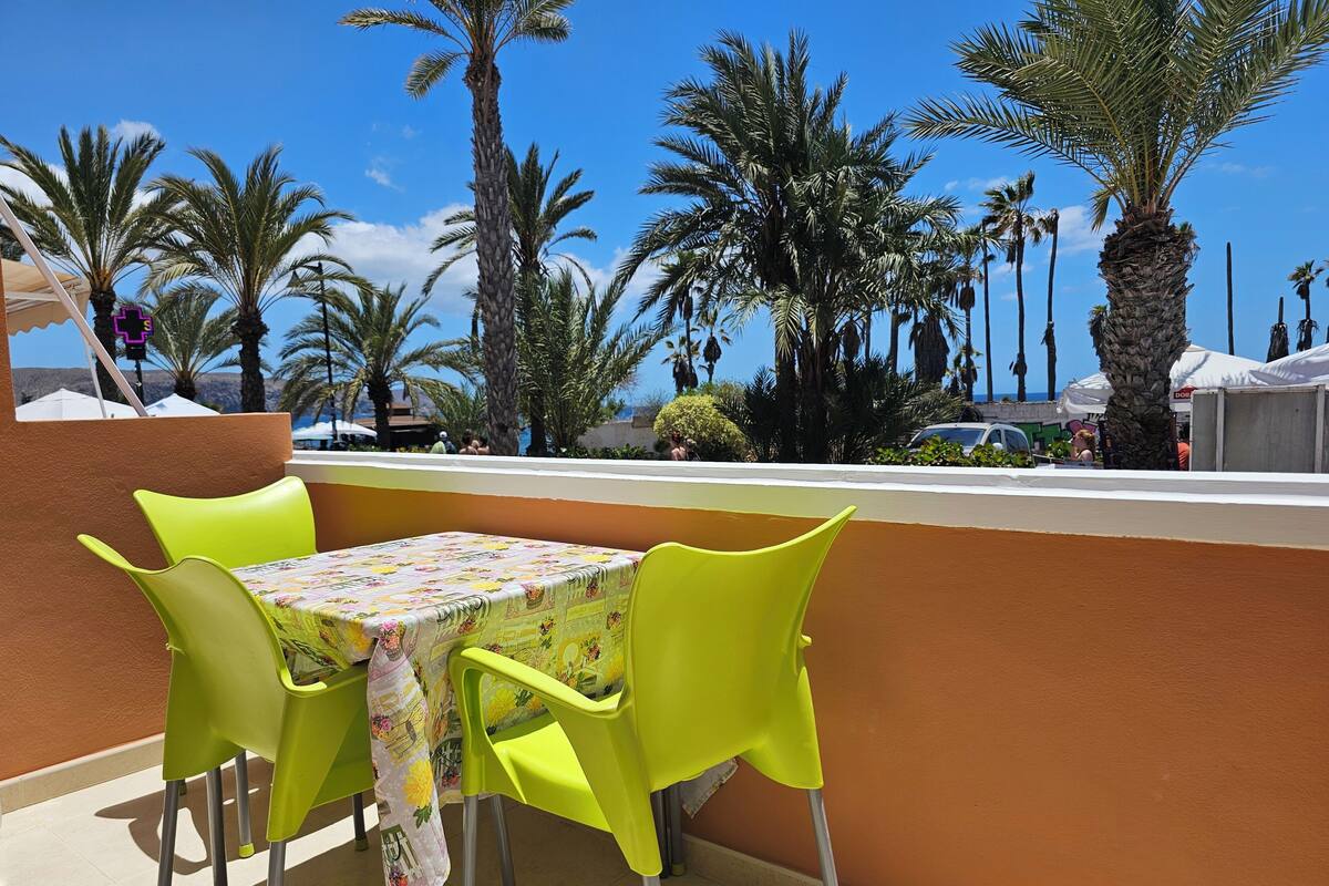 Une terrasse avec une table et des chaises, d’où l’on peut admirer des palmiers et un ciel d’un bleu limpide.