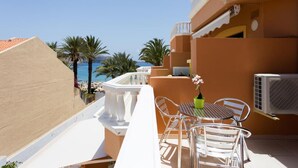 Un balcón con una mesa y sillas, con vista a una playa y palmeras.