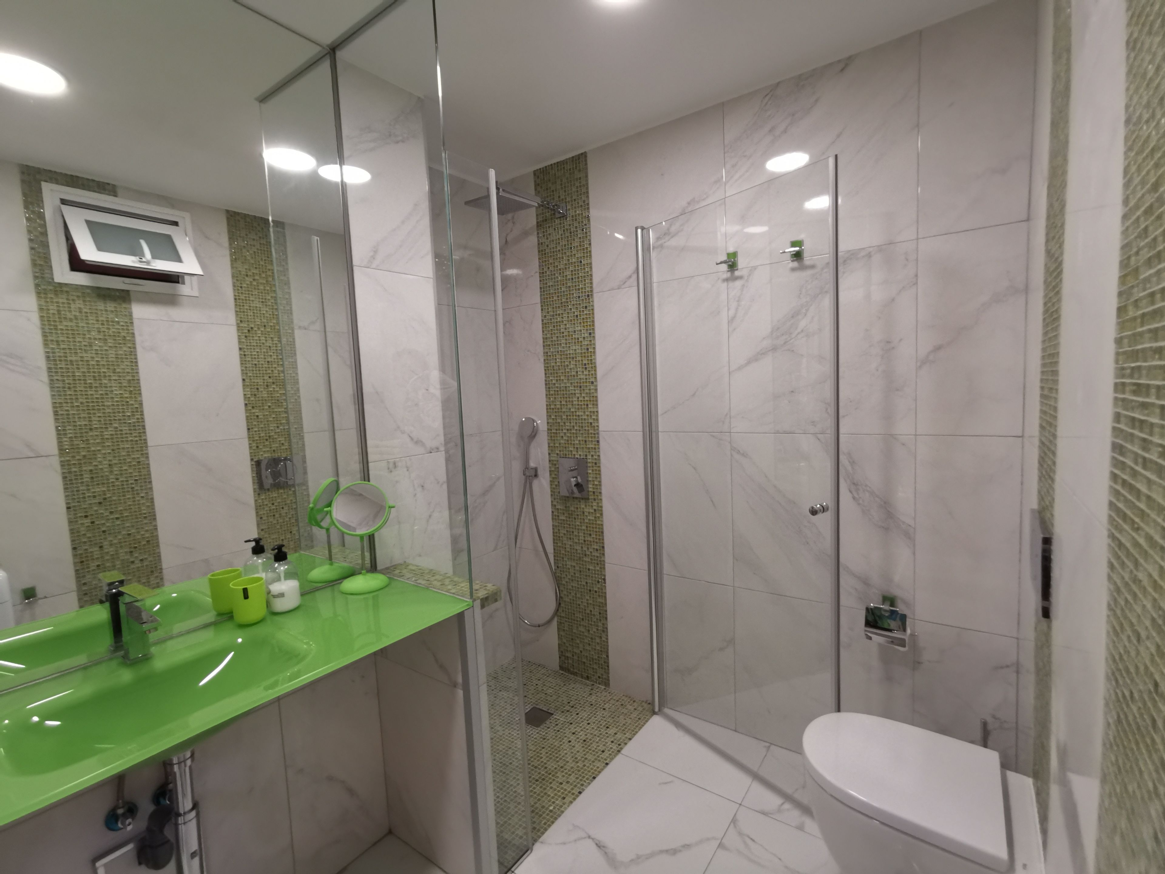 A modern bathroom with a glass-enclosed shower, a green sink, and a toilet.