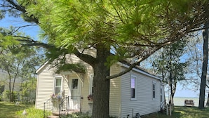 Une maison de plain-pied avec un grand arbre devant, un petit porche et une vue sur l’eau.