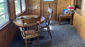 Une cabane en bois avec une table ronde et des chaises, une porte avec une fenêtre et une étagère remplie de livres.