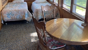 Une chambre de style cabane avec deux lits, une table à manger en bois et de grandes fenêtres.