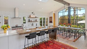 Een moderne keuken met een centraal eiland, barkrukken en een groot raam met uitzicht op groen.