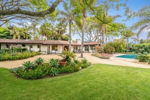 A house with a tiled roof, a swimming pool, and a well-maintained garden with various plants and a lawn. - Expansive and Modern Home With Pool and Tennis Court! (Santa Barbara)