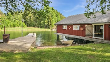 Laituri ulottuu tyynen järven ylle, ja sen vieressä on punainen rakennus.