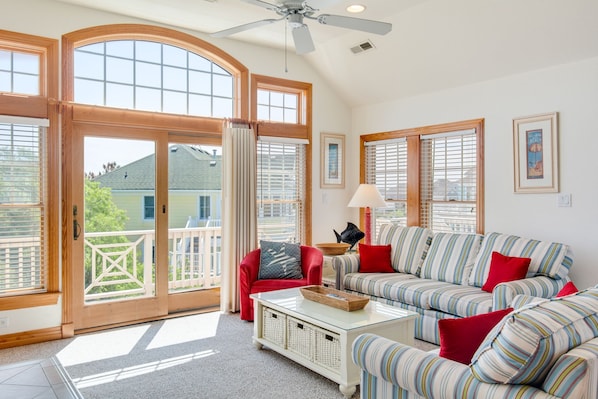 A spacious living room with a large window, a ceiling fan, and a striped sofa with red cushions.