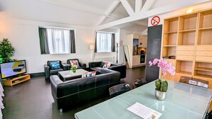 Una sala de estar moderna con un conjunto de sofá, una mesa de centro, un televisor y una mesa de comedor de vidrio con una planta en maceta.
